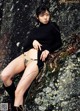 A woman in a black sweater and tan panties sitting on a rock.