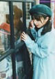 A woman in a blue coat and a green beret looking at a window.