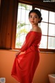 A woman in a red dress standing in front of a window.