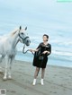 A woman standing next to a white horse on a beach.