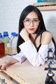 A woman wearing glasses sitting at a table with a microscope.