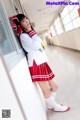 A woman in a school uniform leaning against a wall.