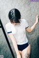 A woman in a white shirt and blue shorts standing in a bathroom.