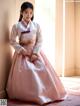 A woman in a pink and white hanbok sitting on the floor.