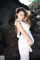 A woman in a white dress standing on a rocky beach.